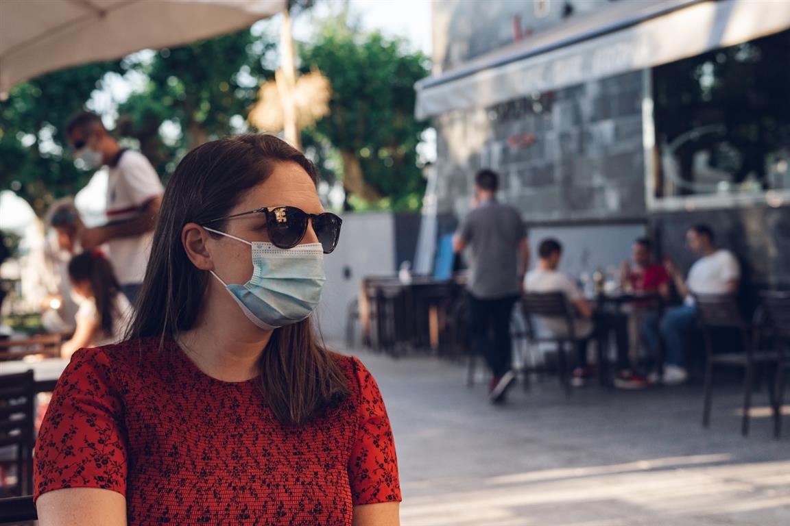 Shallow focus shot of a caucasian female wearing a medical mask and sunglasses sitting in a cafe - Credit: Wirestock | Freepik